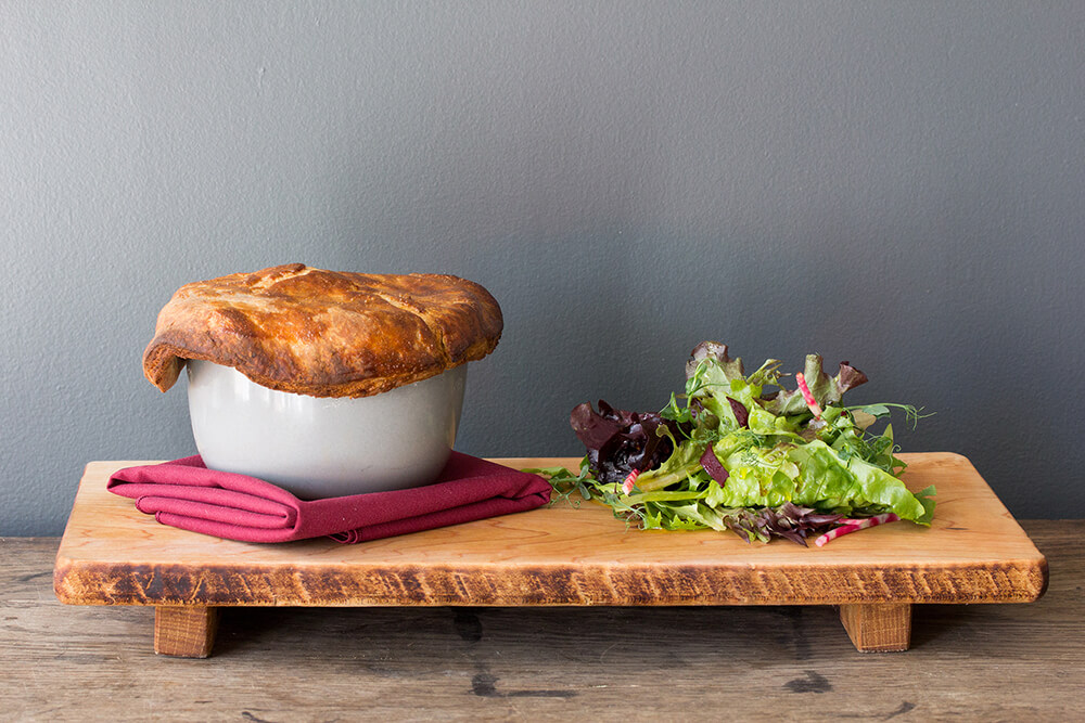Chicken pot pie and mixed greens on a wooden board in front of a grey wall