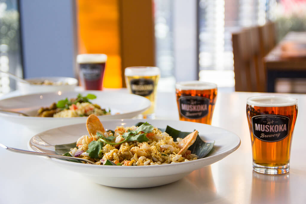 A diagonal lineup of Muskoka Brewery Beers in front of different Canteen dishes.