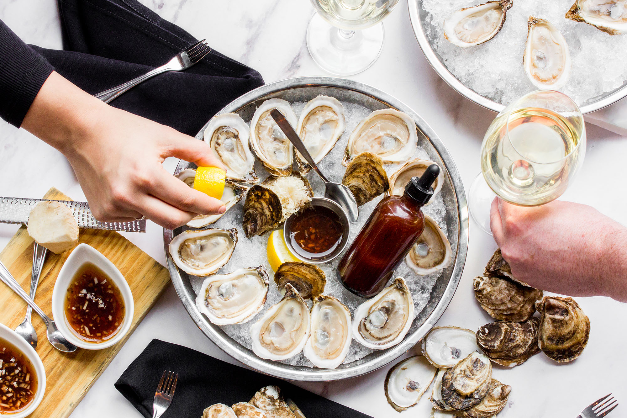 A tablescape with oysters and wine, with one hand grabbing an oyster from the tray.