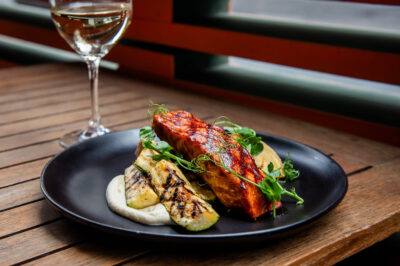 Barbequed Salmon on wooden table in front of out of focus glass of white wine