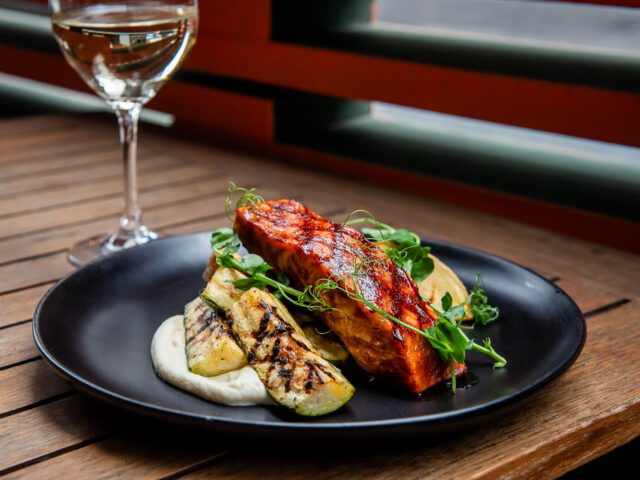 Barbequed Salmon on wooden table in front of out of focus glass of white wine