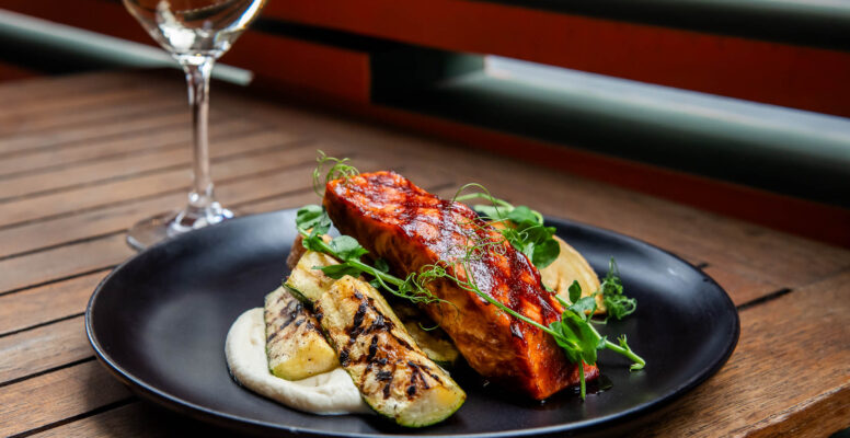 Barbequed Salmon on wooden table in front of out of focus glass of white wine
