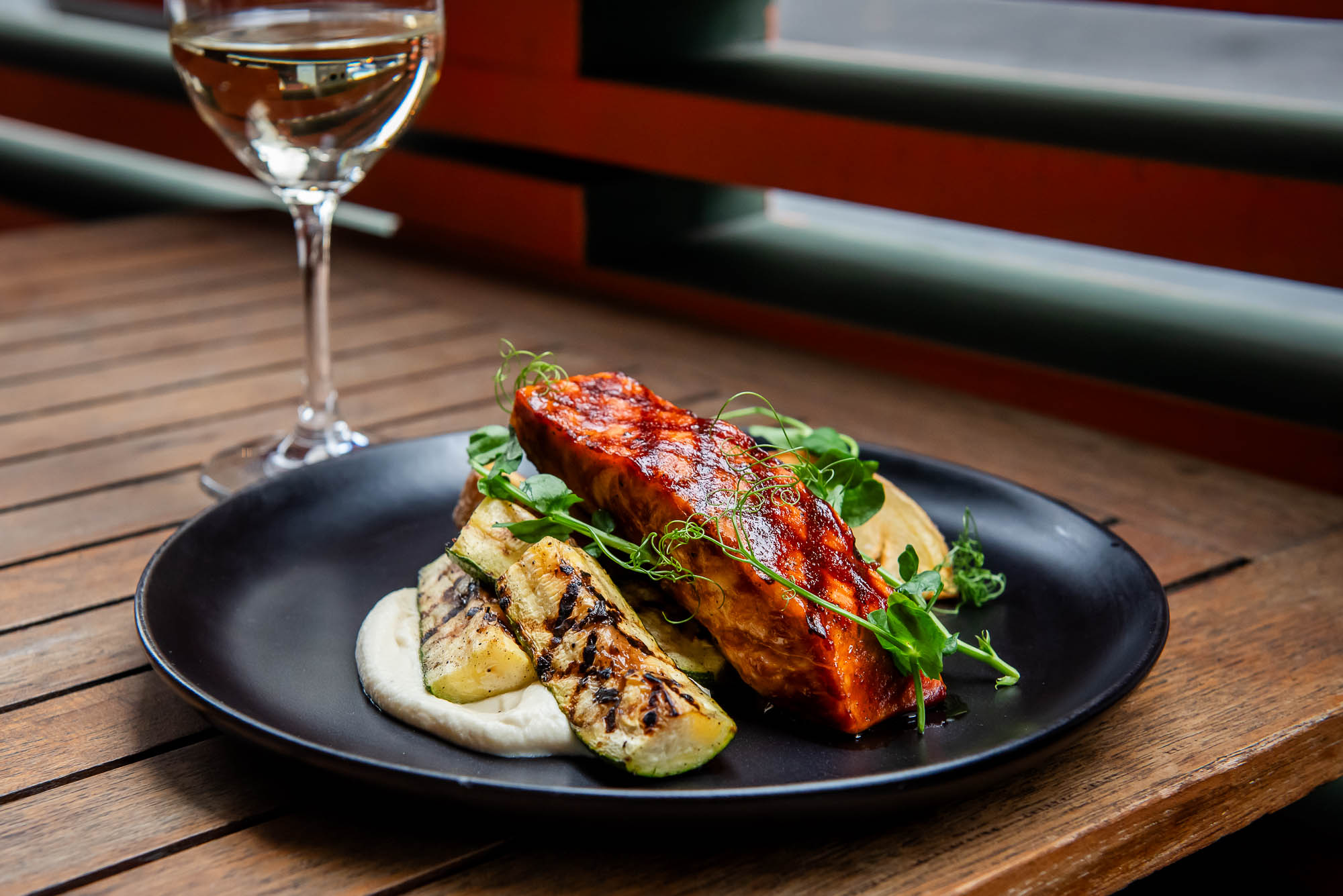 Barbequed Salmon on wooden table in front of out of focus glass of white wine