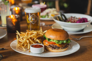 the guild burger sits on white plate with fries and ramekin of ketchup