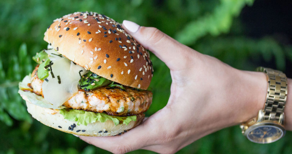 Teriyaki Salmon Burger held in front of greenery.