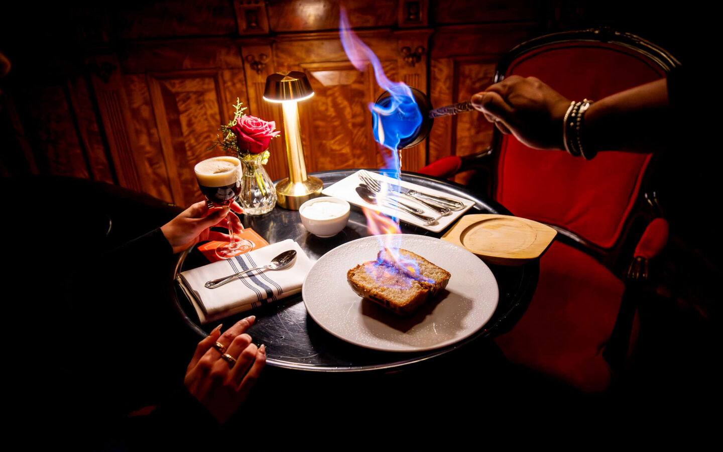 Flaming baba au rhum being prepared tableside with dramatic blue flames, alongside cocktails and elegant table setting