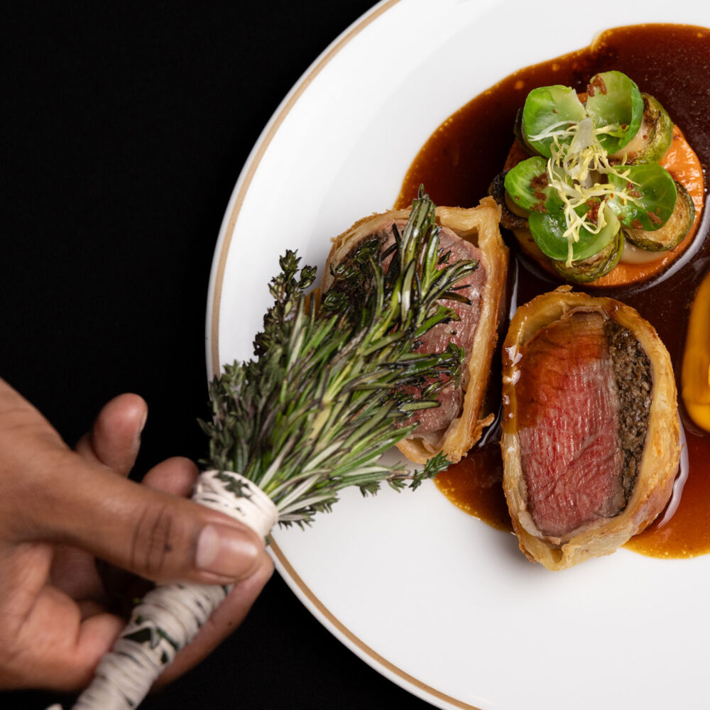 Sliced beef Wellington with medium-rare beef in golden pastry, served with rich brown sauce, roasted vegetables, and fresh herbs