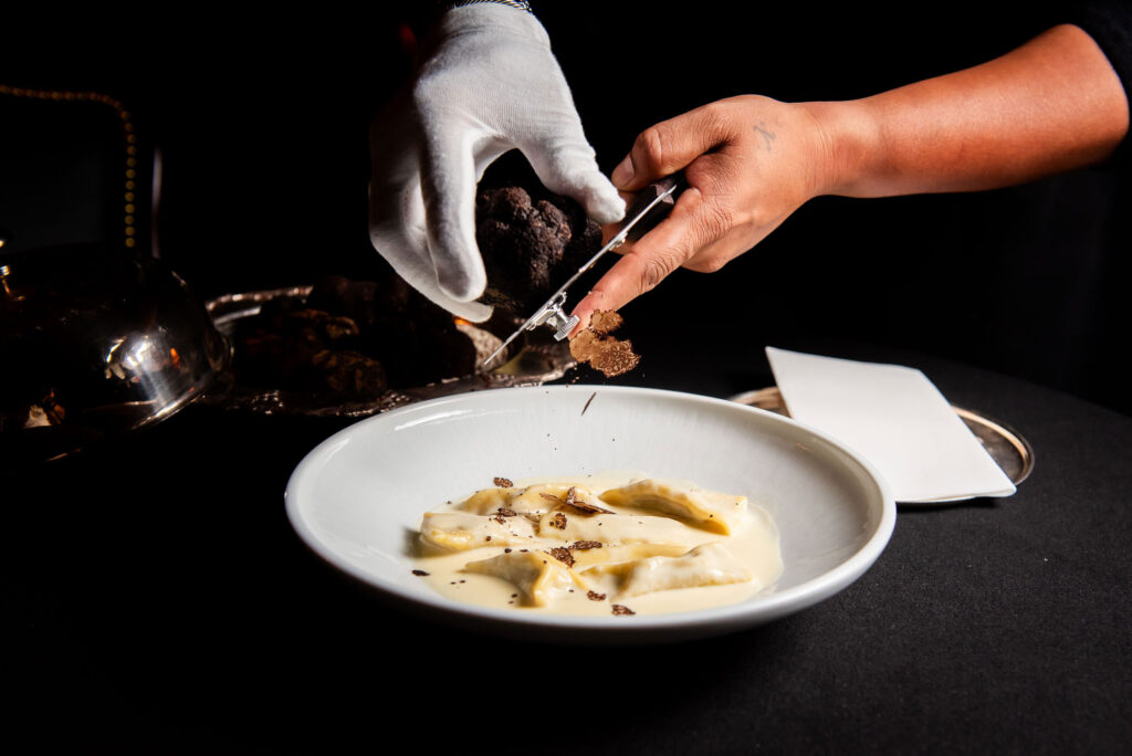 a person shaving a truffle over a pasta dish