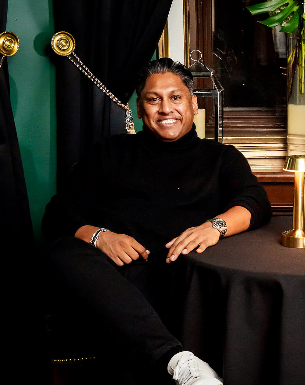 Chef Kevin Ramasawmy seated in elegant restaurant setting with green velvet curtains and gold accents