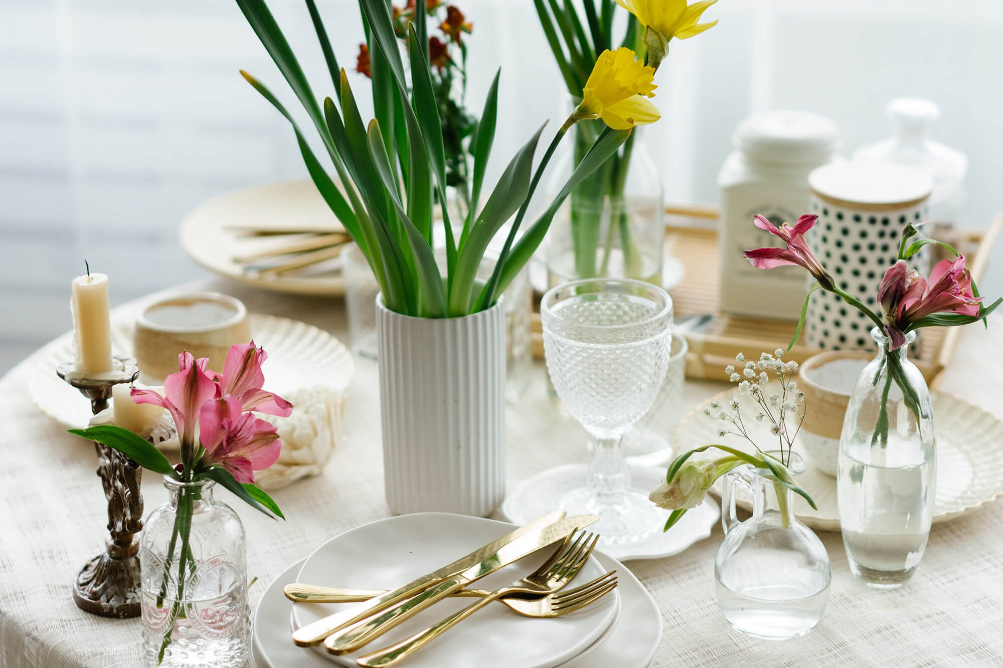 a table topped with a vase filled with flowers, candles, plates and glassware