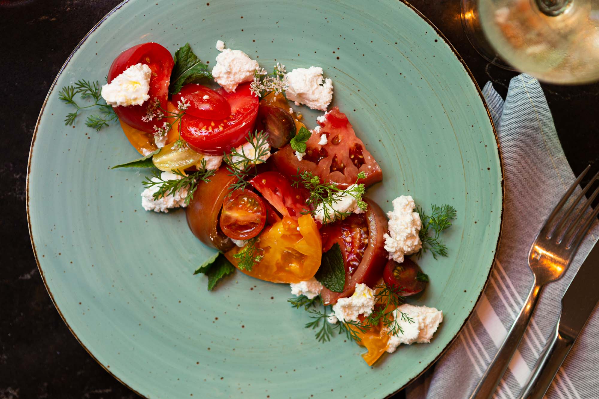 Babel's heirloom tomato salad with gerens and feta on a turquoise plate. Bird's eye shot.