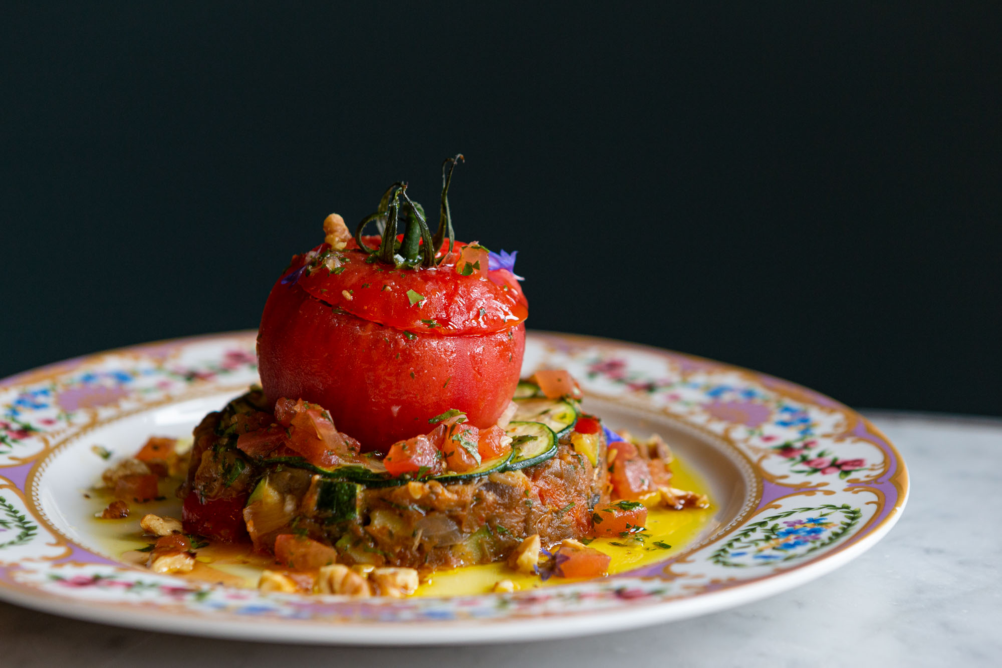 Tomate farcie (ratatouille with a large, bright red tomato on top) on a decorative plate. Medium straight-on shot.