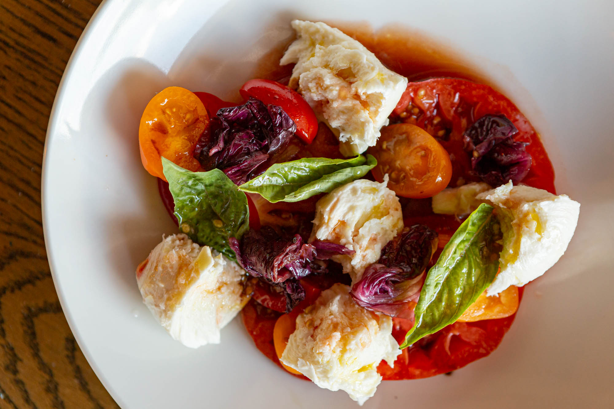 Top-down view of Parcheggio's tomato Caprese with red and orange tomatoes, basil leaves, and cheese on a white plate.