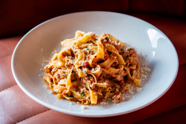 TAGLIATELLE BOLOGNESE in white bowl on red leather chair