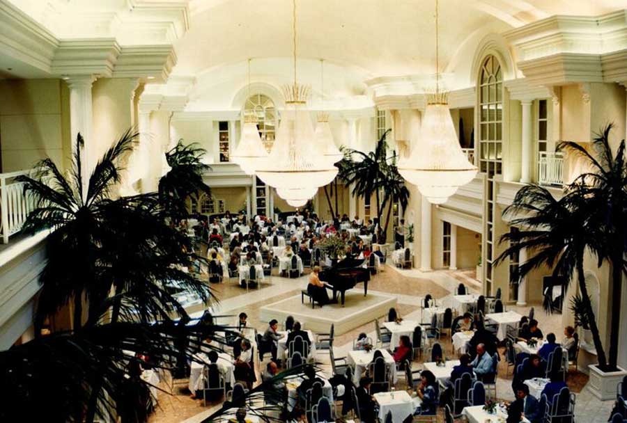 the old arcadian court venue with large crystal chandeliers and a grand piano in the middle of seating