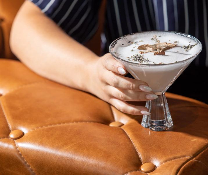 Hand holding a martini on the arm of a brown tufted leather chair