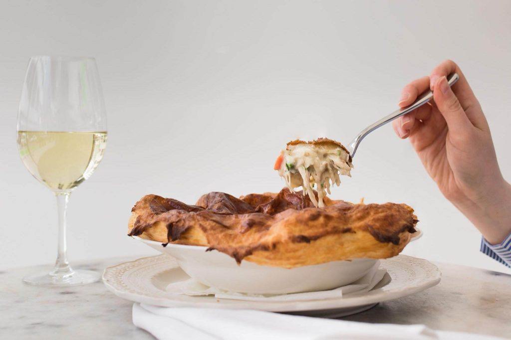person eating chicken pot pie with a fork with a glass of white wine
