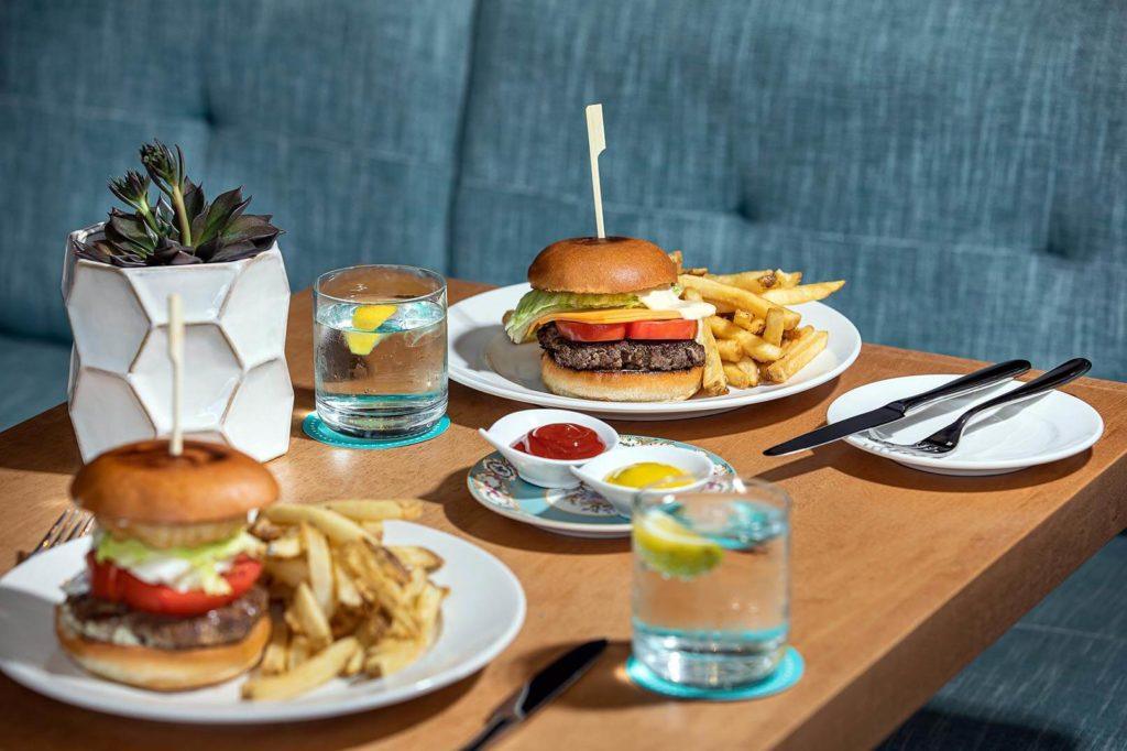 Two beef burgers on a table with condiments, water and succulent