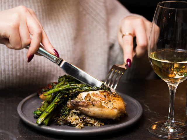 guest eating chicken with a glass of white wine