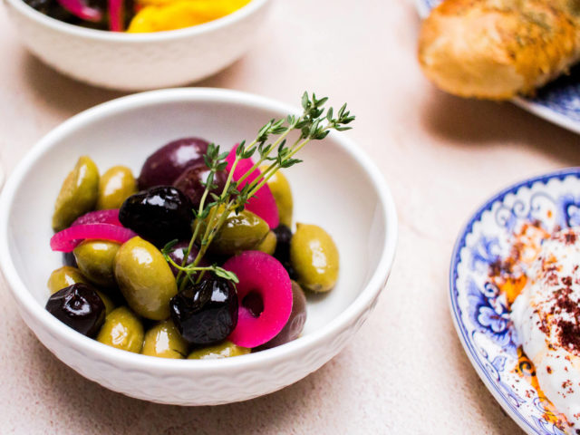 small white bowl of black and green olives, garnished with thyme