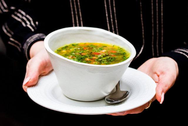 Bowl of mushroom and lentil soup being held by a woman in a black shirt