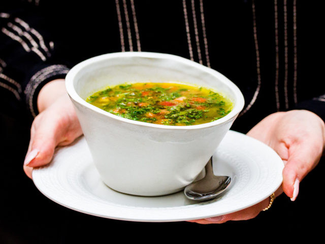 Bowl of mushroom and lentil soup being held by a woman in a black shirt