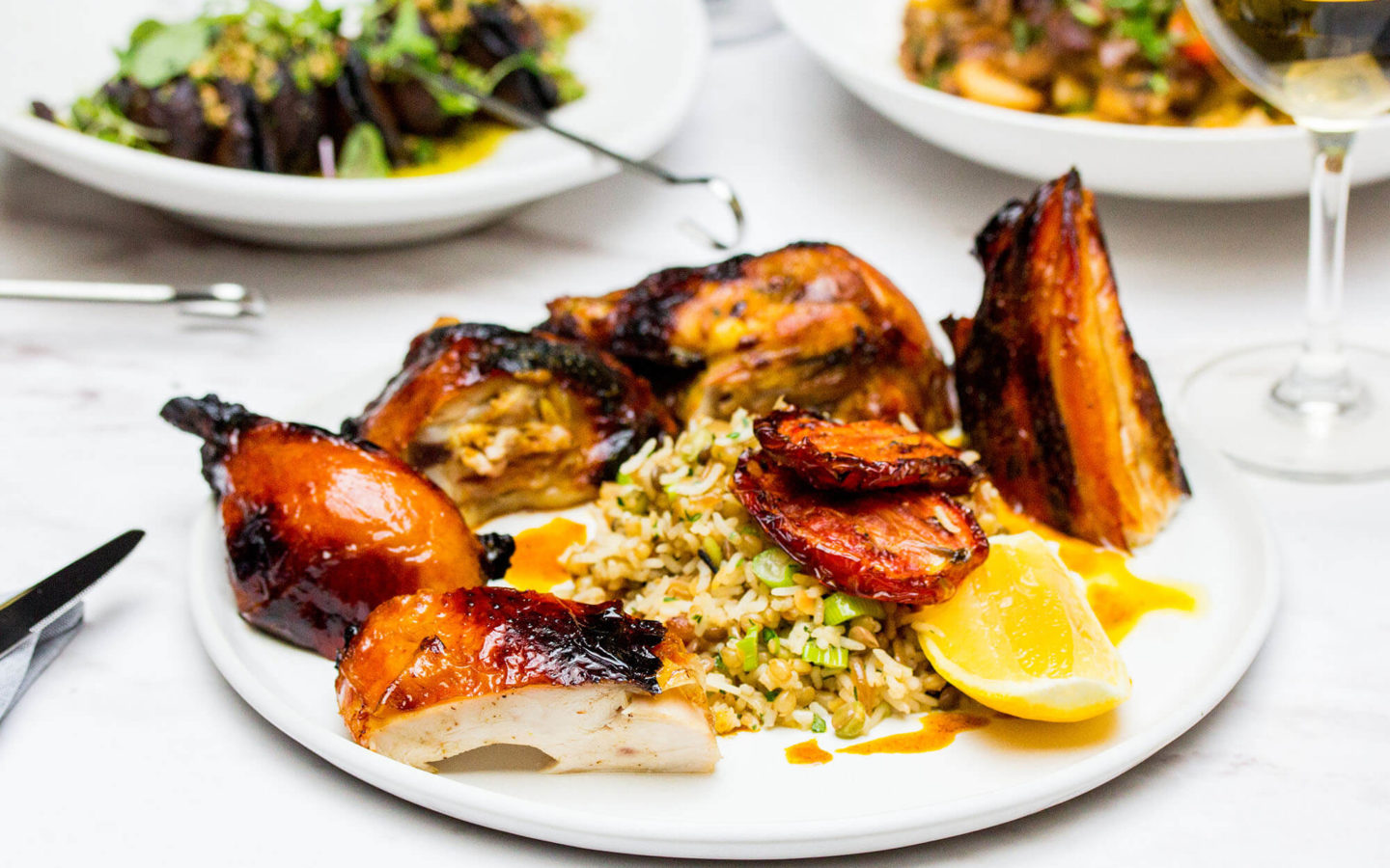 grilled spiced half chicken served with rice, grain and ginger pilaf, on a table with other dinner plates in the background