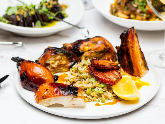 grilled spiced half chicken served with rice, grain and ginger pilaf, on a table with other dinner plates in the background