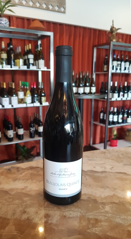 Domaine Joncy Beaujolais Quincié Quartz wine bottle on wood tabletop in front of shelves with wine bottles