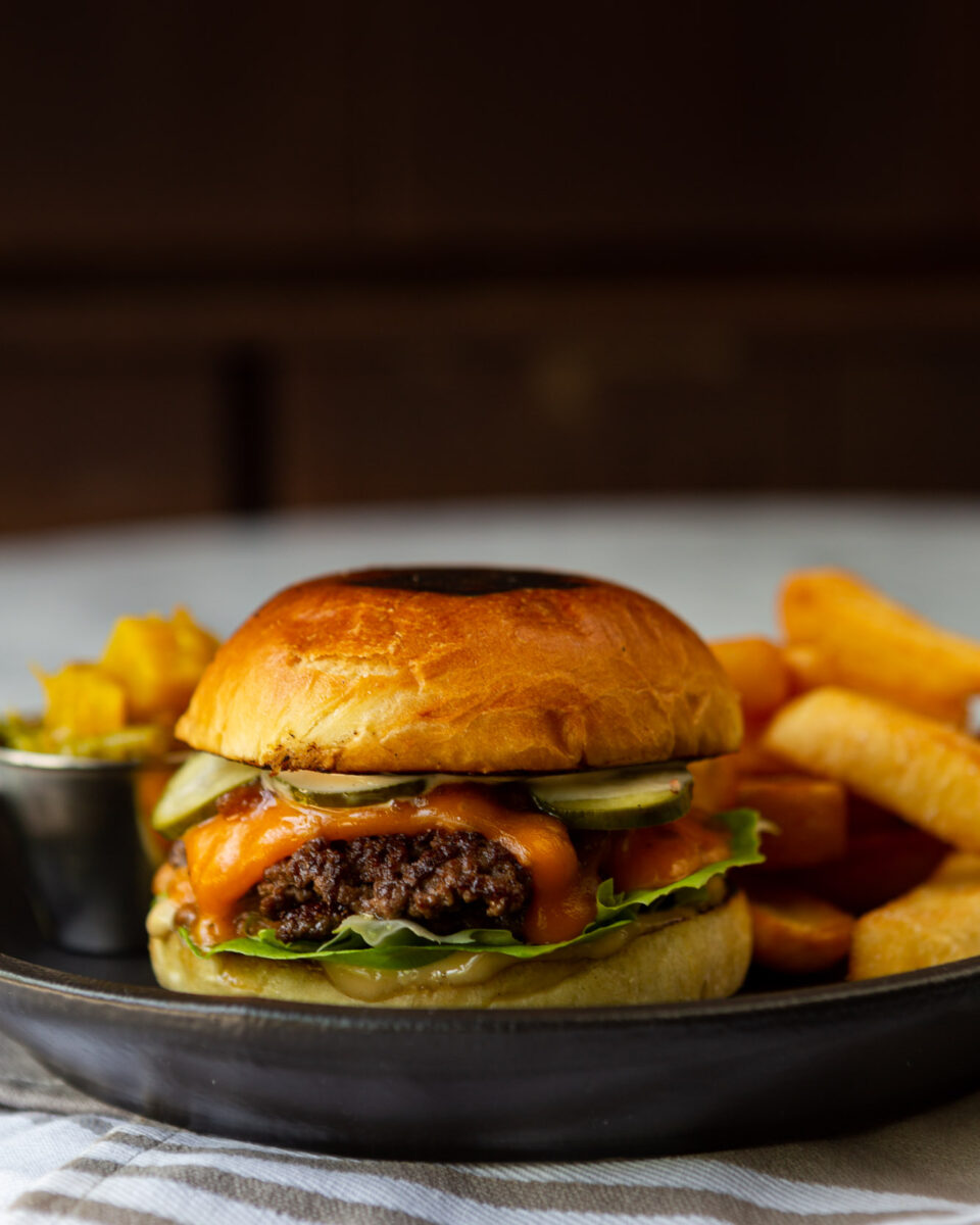 The Rabbit Hole burger with a side of fries on a dark stone plate